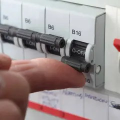 A finger flips a circuit breaker switch to the OFF position. This action might be taken if a circuit breaker fuse blown, indicating an overload or fault.