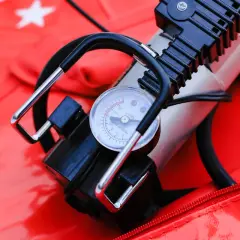 A portable air pump with a pressure gauge sits on a red surface with snowflake patterns. This compact device is a handy air compressor for quick inflation needs.