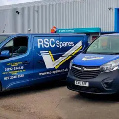 Two blue vans from T&B Motors, branded RSC Spares, are parked outside a warehouse.