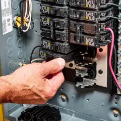Hand removing a circuit breaker from an electrical panel, illustrating a breaker fuse replacement.