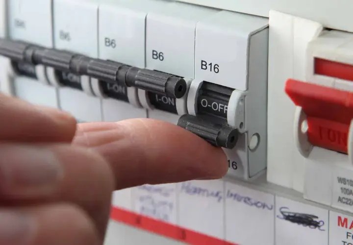 A finger flips a circuit breaker switch to the OFF position. This action might be taken if a circuit breaker fuse blown, indicating an overload or fault.