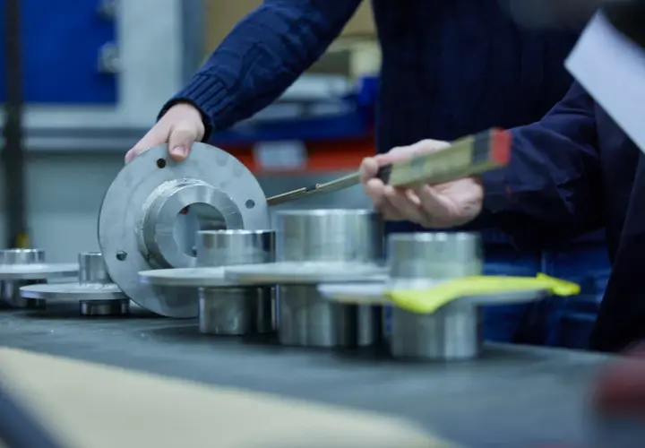 Hands examine metal components, possibly for a fluid power equation application, with a ruler for measurement.