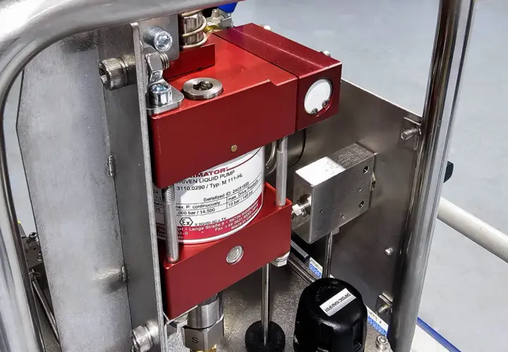 Close-up of a red liquid pump, likely a pneumatic pump, mounted on a stainless steel frame.