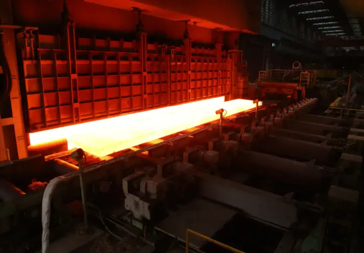 A glowing hot steel slab moves through a TMEIC Corporation industrial furnace, ready for processing.