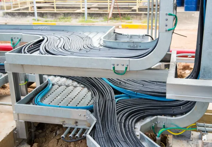 A complex network of black and blue cables is neatly organized within metal tray cable systems, showcasing industrial cable management.