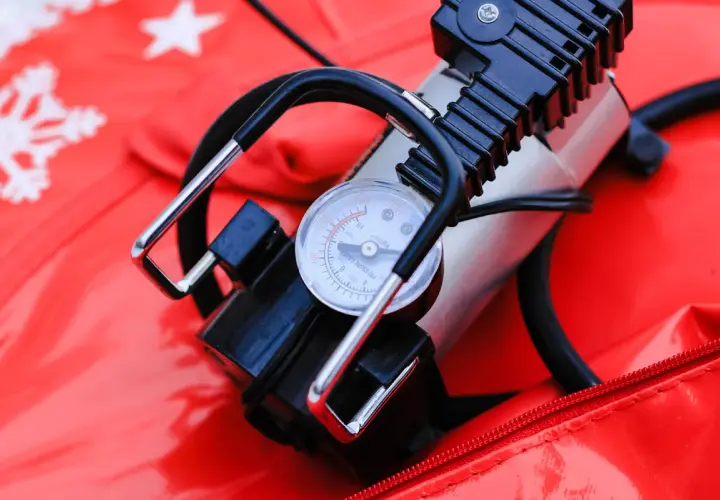 A portable air pump with a pressure gauge sits on a red surface with snowflake patterns. This compact device is a handy air compressor for quick inflation needs.