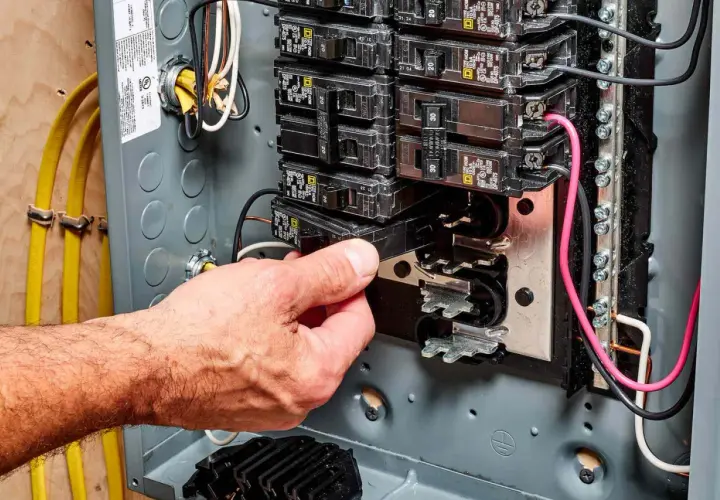 Hand removing a circuit breaker from an electrical panel, illustrating a breaker fuse replacement.