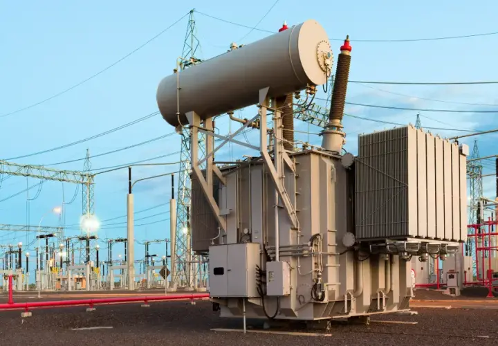 A substation with large transformers, which handle power in kilovolts, under a twilight sky.