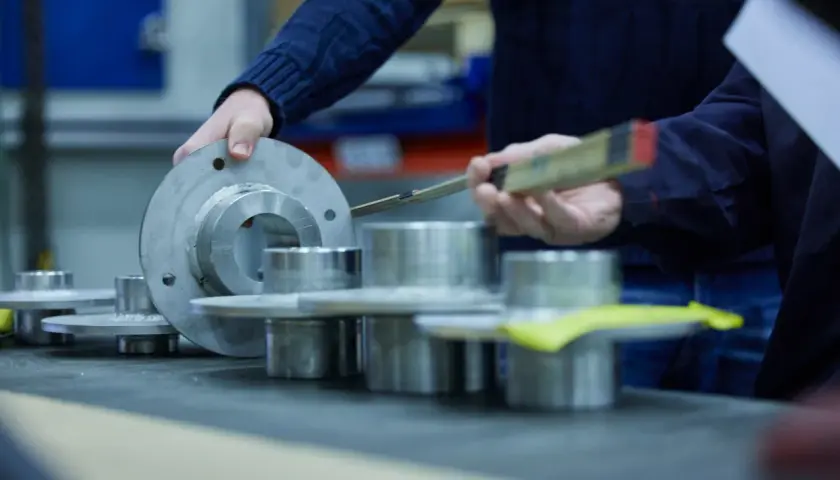 Hands examine metal components, possibly for a fluid power equation application, with a ruler for measurement.
