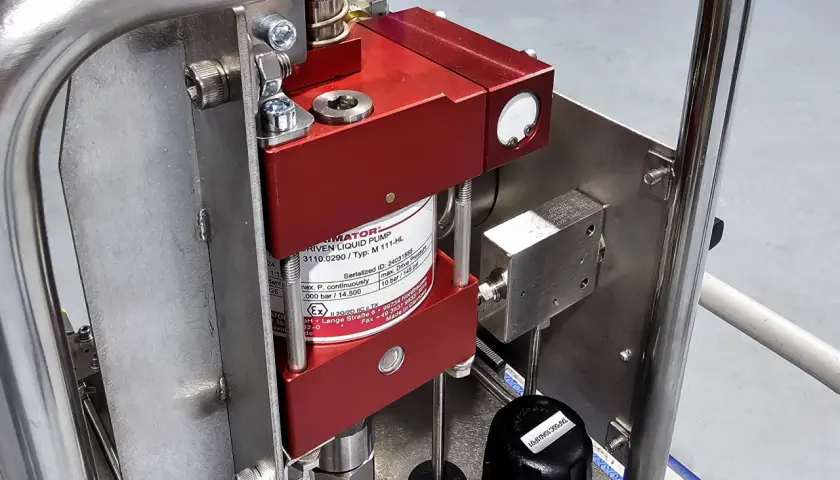 Close-up of a red liquid pump, likely a pneumatic pump, mounted on a stainless steel frame.