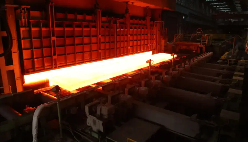 A glowing hot steel slab moves through a TMEIC Corporation industrial furnace, ready for processing.