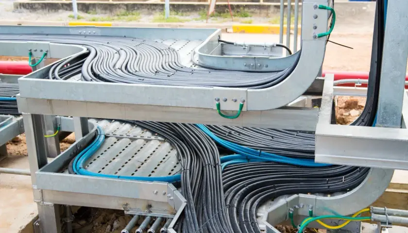 A complex network of black and blue cables is neatly organized within metal tray cable systems, showcasing industrial cable management.