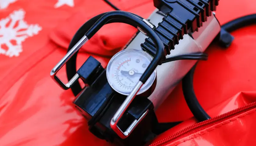 A portable air pump with a pressure gauge sits on a red surface with snowflake patterns. This compact device is a handy air compressor for quick inflation needs.