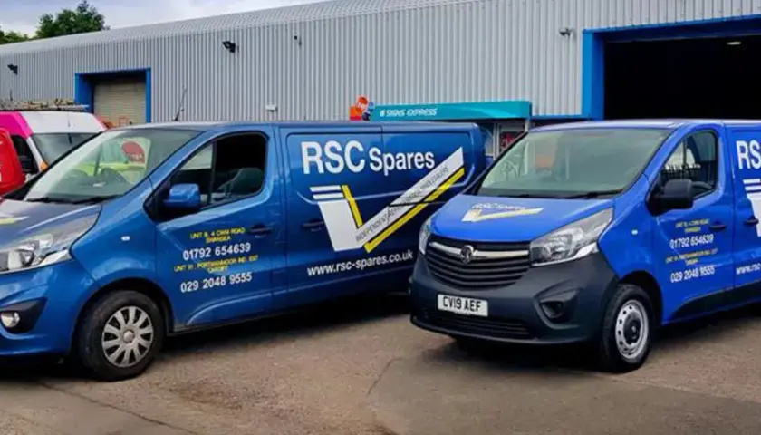 Two blue vans from T&B Motors, branded RSC Spares, are parked outside a warehouse.
