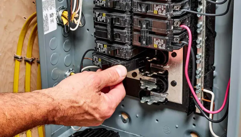 Hand removing a circuit breaker from an electrical panel, illustrating a breaker fuse replacement.