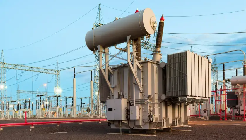 A substation with large transformers, which handle power in kilovolts, under a twilight sky.
