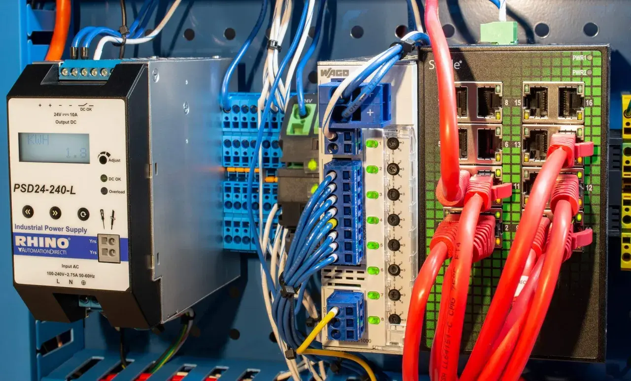 Industrial power supply and network switch components, part of a protective distribution system, with red Ethernet cables connected.