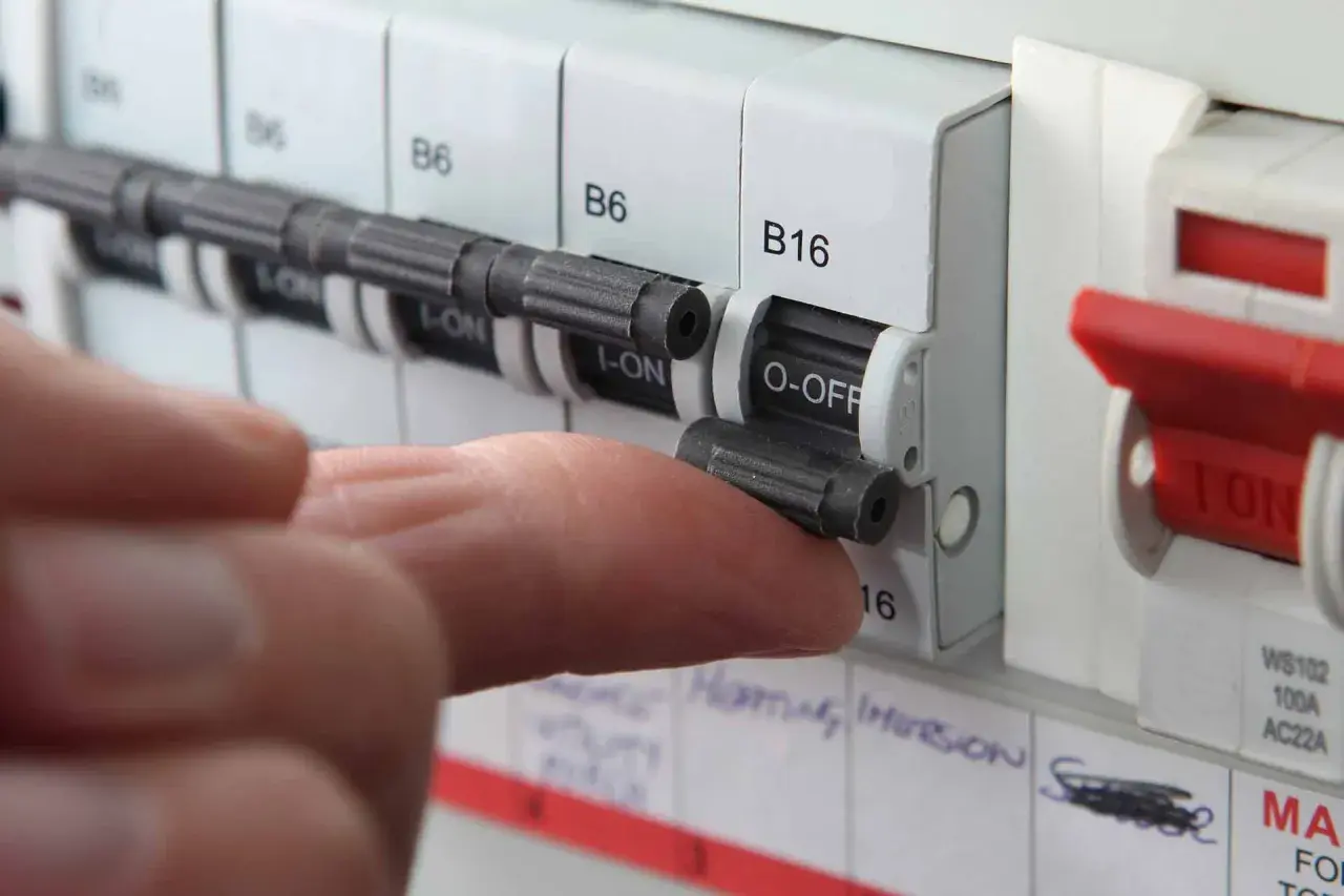 A finger flips a circuit breaker switch to the OFF position. This action might be taken if a circuit breaker fuse blown, indicating an overload or fault.