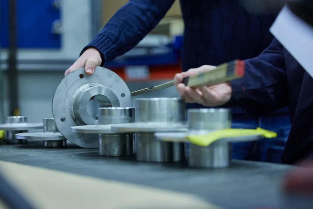 Hands examine metal components, possibly for a fluid power equation application, with a ruler for measurement.