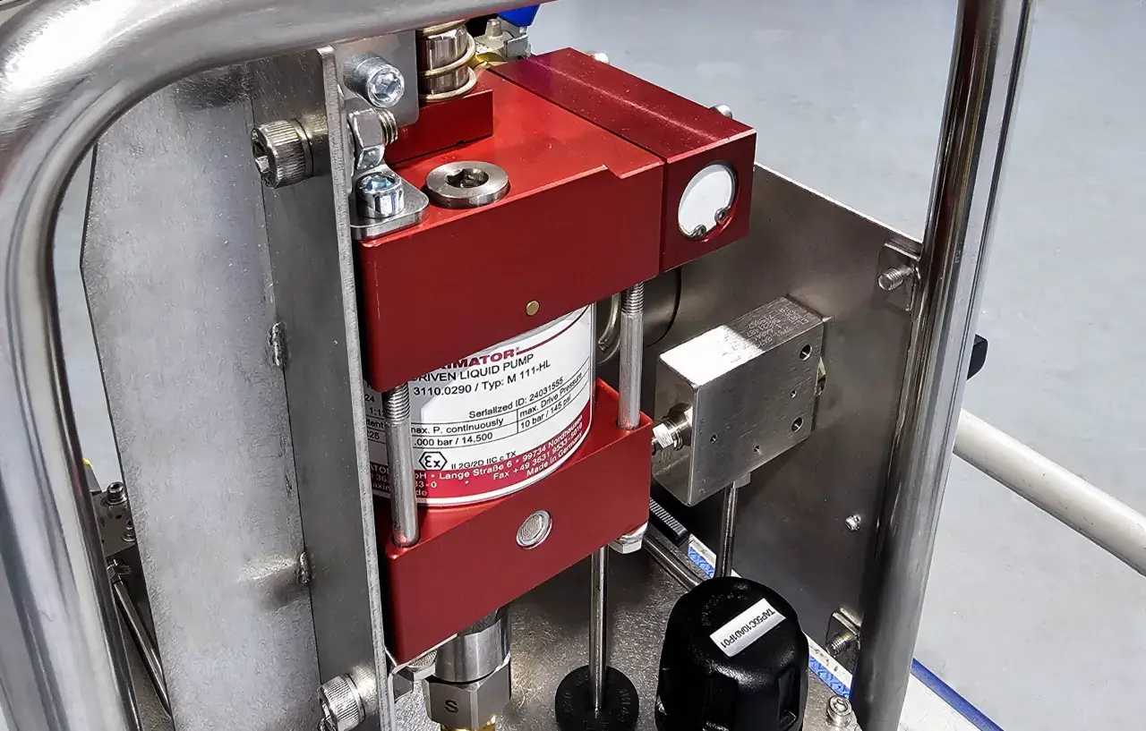 Close-up of a red liquid pump, likely a pneumatic pump, mounted on a stainless steel frame.