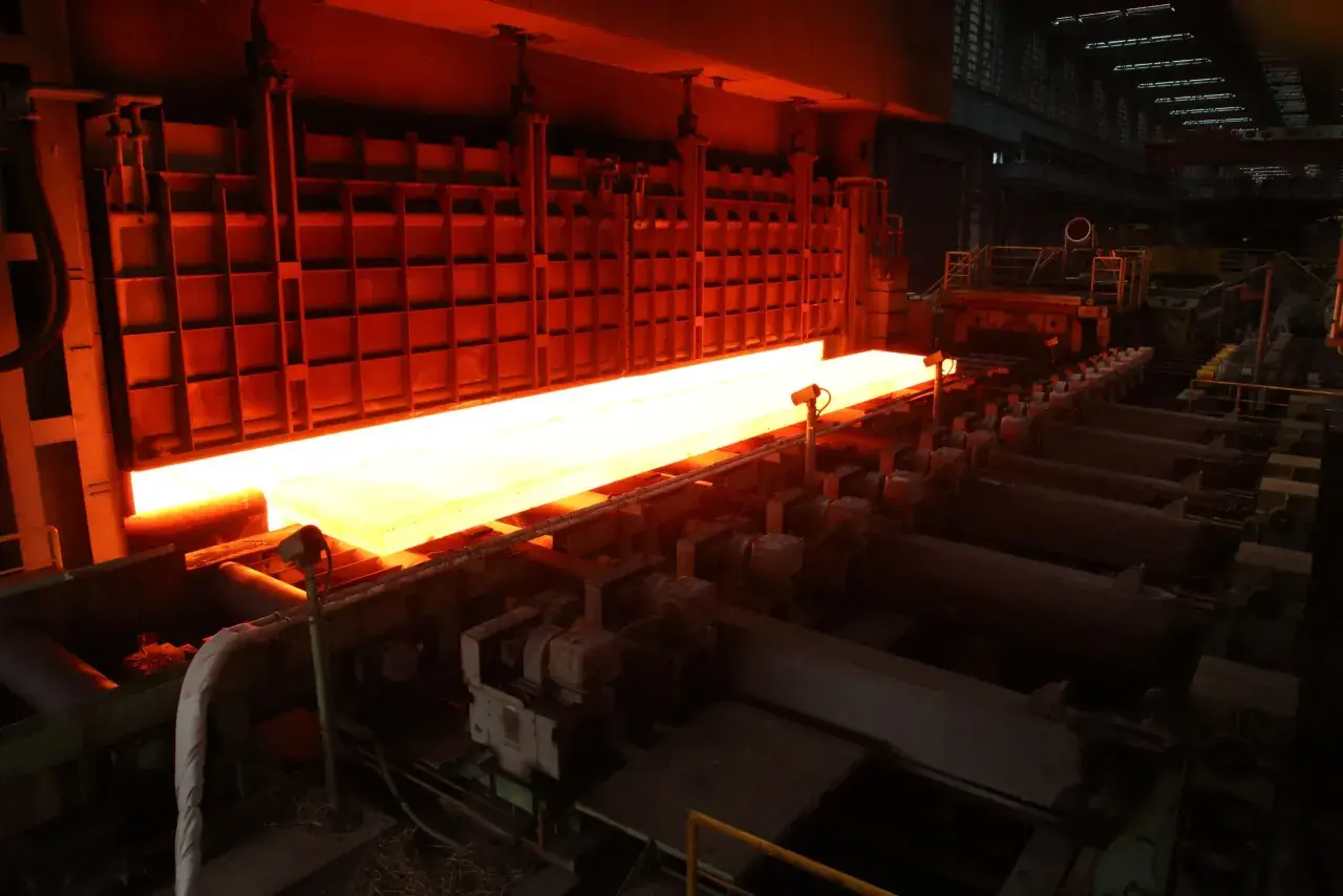 A glowing hot steel slab moves through a TMEIC Corporation industrial furnace, ready for processing.