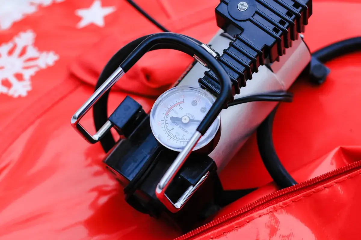 A portable air pump with a pressure gauge sits on a red surface with snowflake patterns. This compact device is a handy air compressor for quick inflation needs.