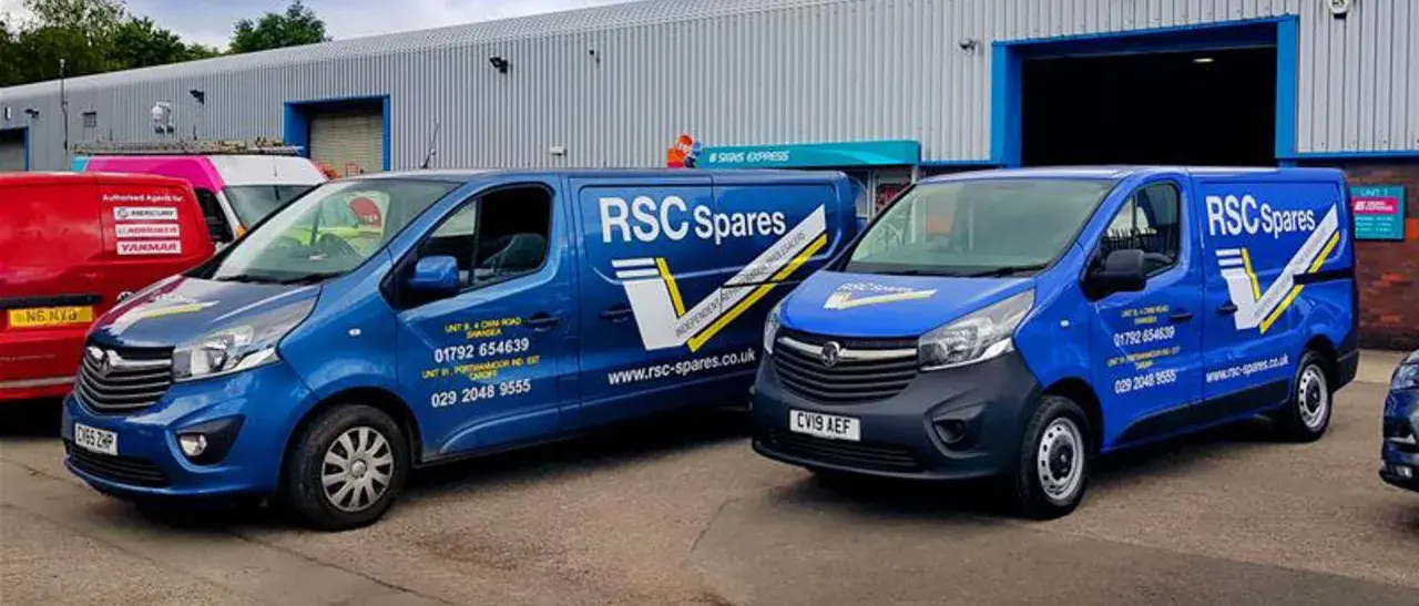 Two blue vans from T&B Motors, branded RSC Spares, are parked outside a warehouse.