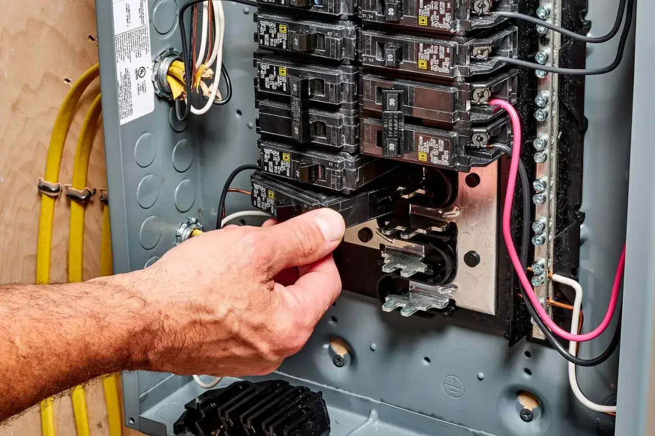 Hand removing a circuit breaker from an electrical panel, illustrating a breaker fuse replacement.