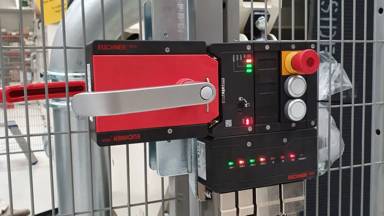 A red and silver Euchner MGB safety handle lock is mounted on a metal cage. The control unit shows green and red indicator lights.