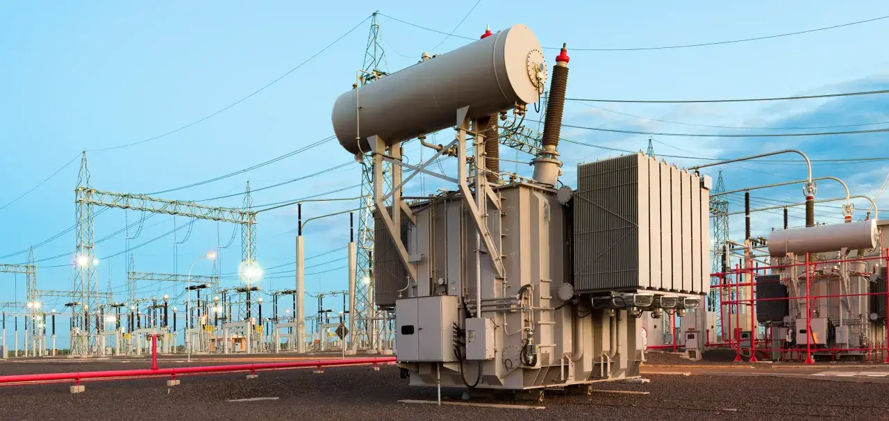A substation with large transformers, which handle power in kilovolts, under a twilight sky.