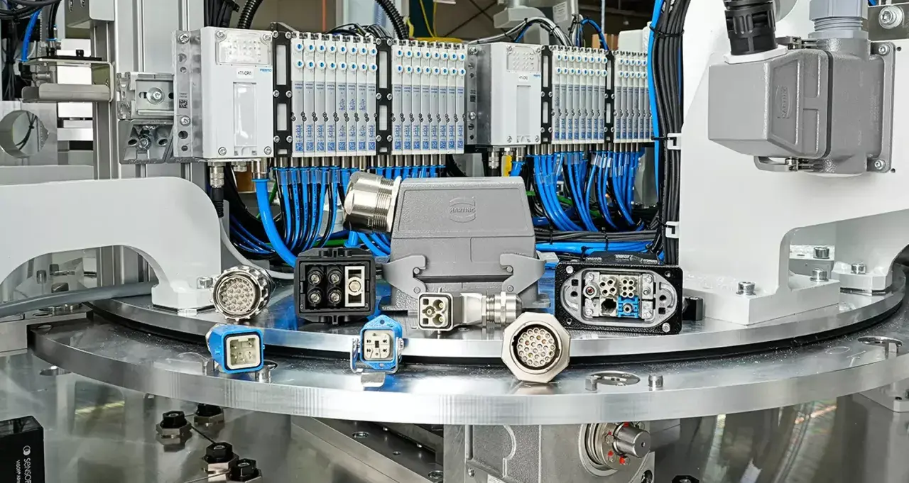 A collection of industrial connectors, including a large grey HARTING connector, are displayed on a metallic surface, with a background of pneumatic valves and wiring.