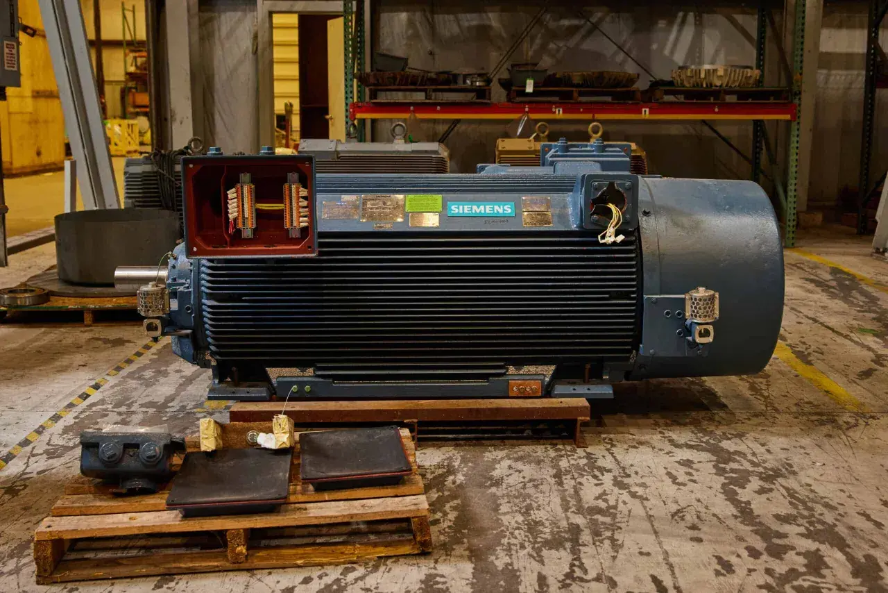 A large Siemens motor with its terminal box open, revealing wiring. Different motor enclosure types are visible in the background.
