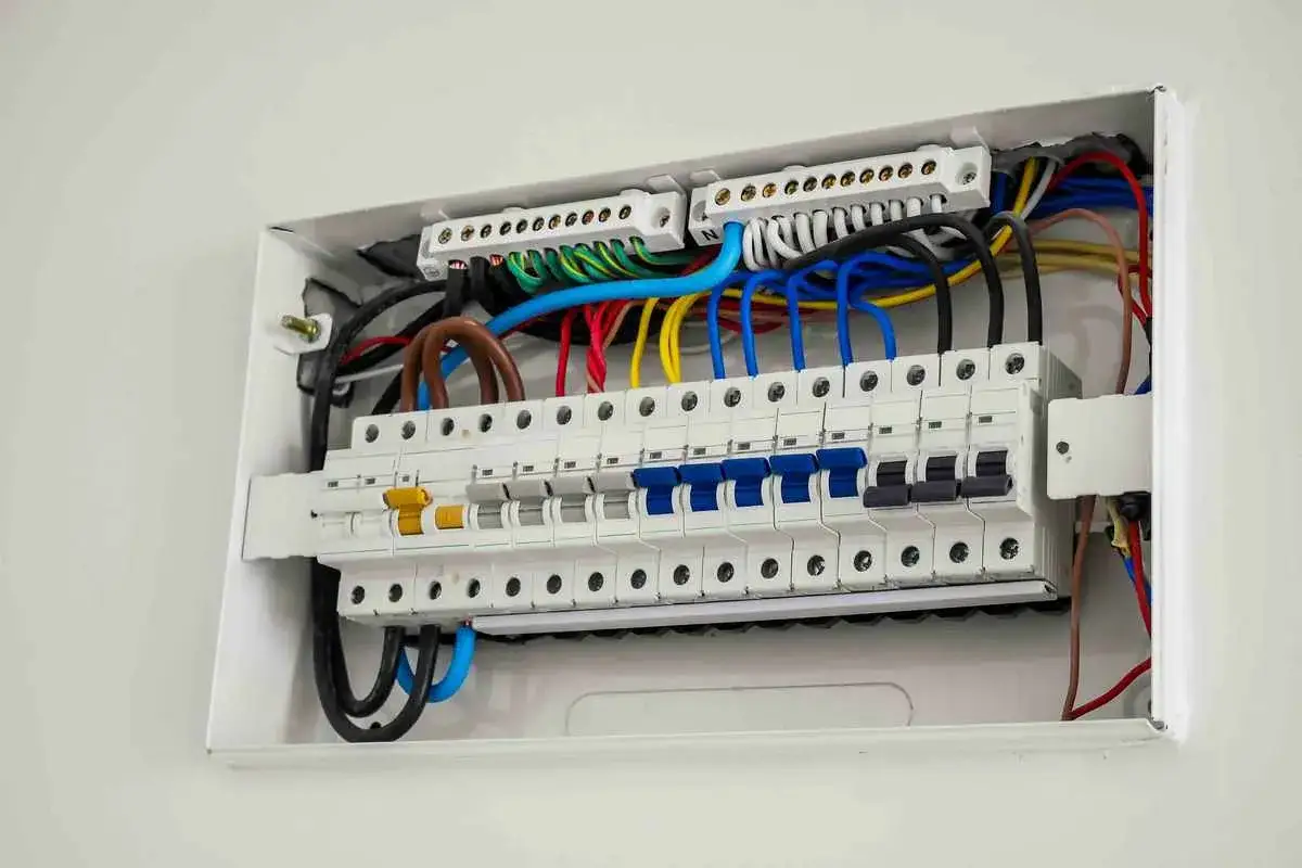 Inside a white electrical panel, rows of circuit breakers are neatly wired. These breakers, unlike older fuse boxes, automatically trip to prevent overloads, answering the question: do breakers have fuses?