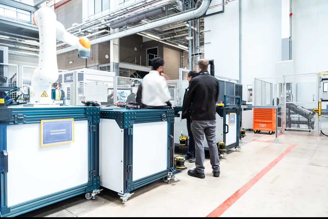 A white robotic arm is part of a collaborative development setup. People observe the adapta robotics in a modern facility.