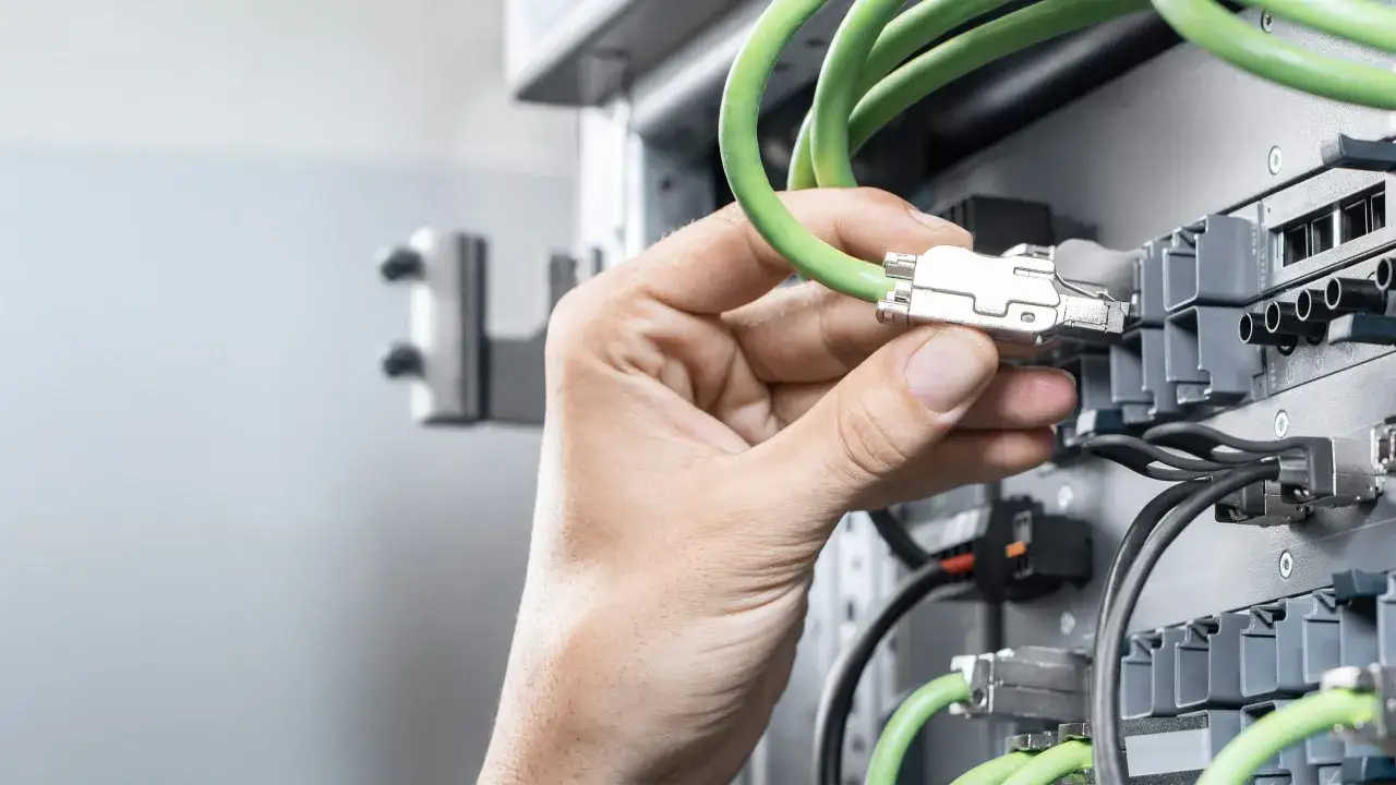 A hand connects a green cable to a Siemens PROFINET device, showcasing industrial network connectivity.