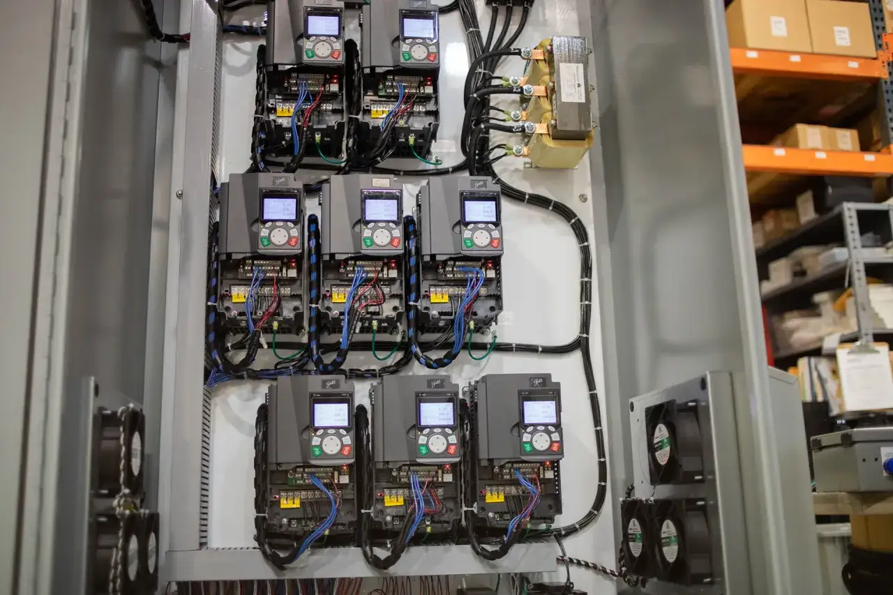 A bank of six variable frequency drives, each with a digital display and controls, are mounted in a control panel. These drives are connected to a transformer and are part of a system that manages output load reactors.