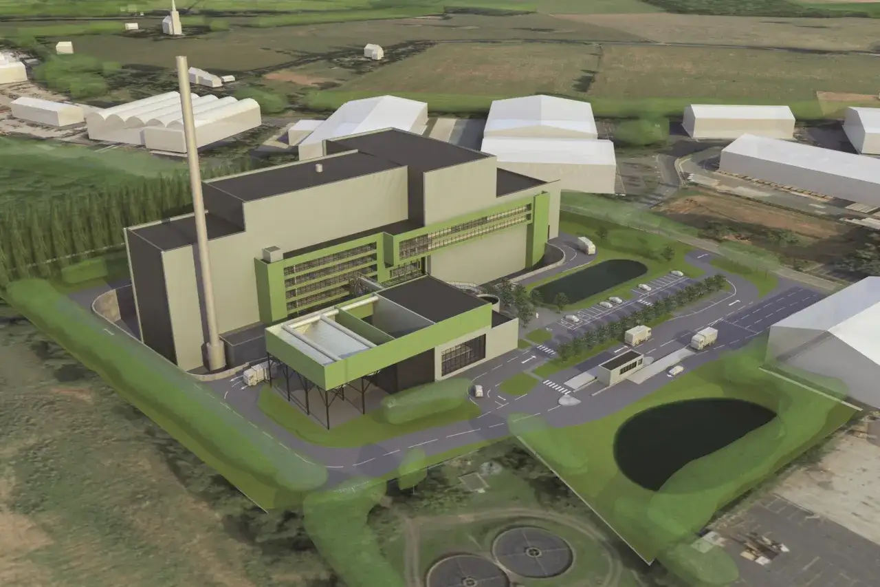 An aerial view of a modern industrial facility, possibly a waste-to-energy plant, designed by Valmet Inc. The complex features a tall smokestack, large grey and green buildings, a parking lot with trucks, and surrounding green spaces.