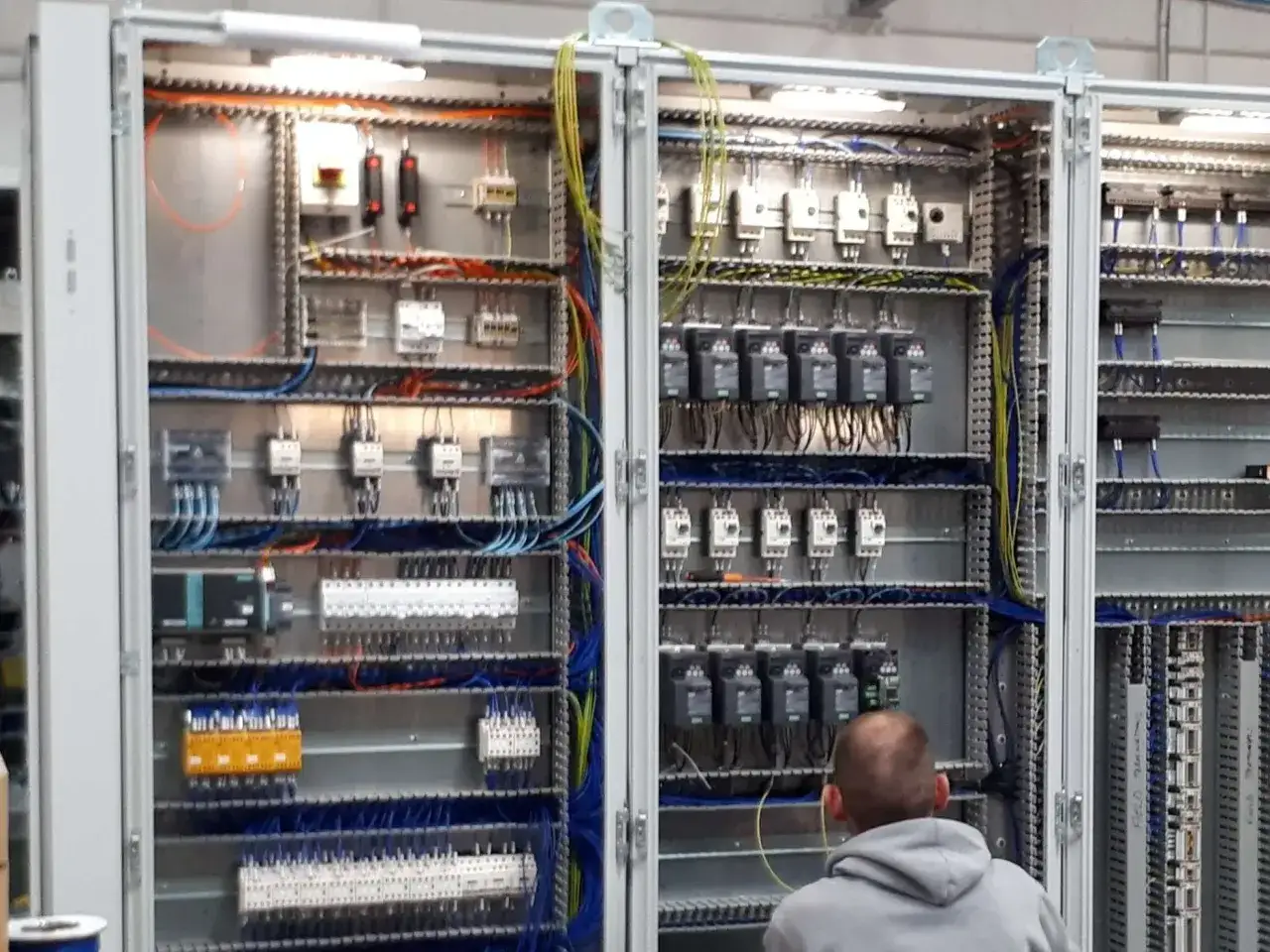 A technician works on a complex electrical panel, a testament to heitek automation. The panel is filled with intricate wiring, relays, and control modules.