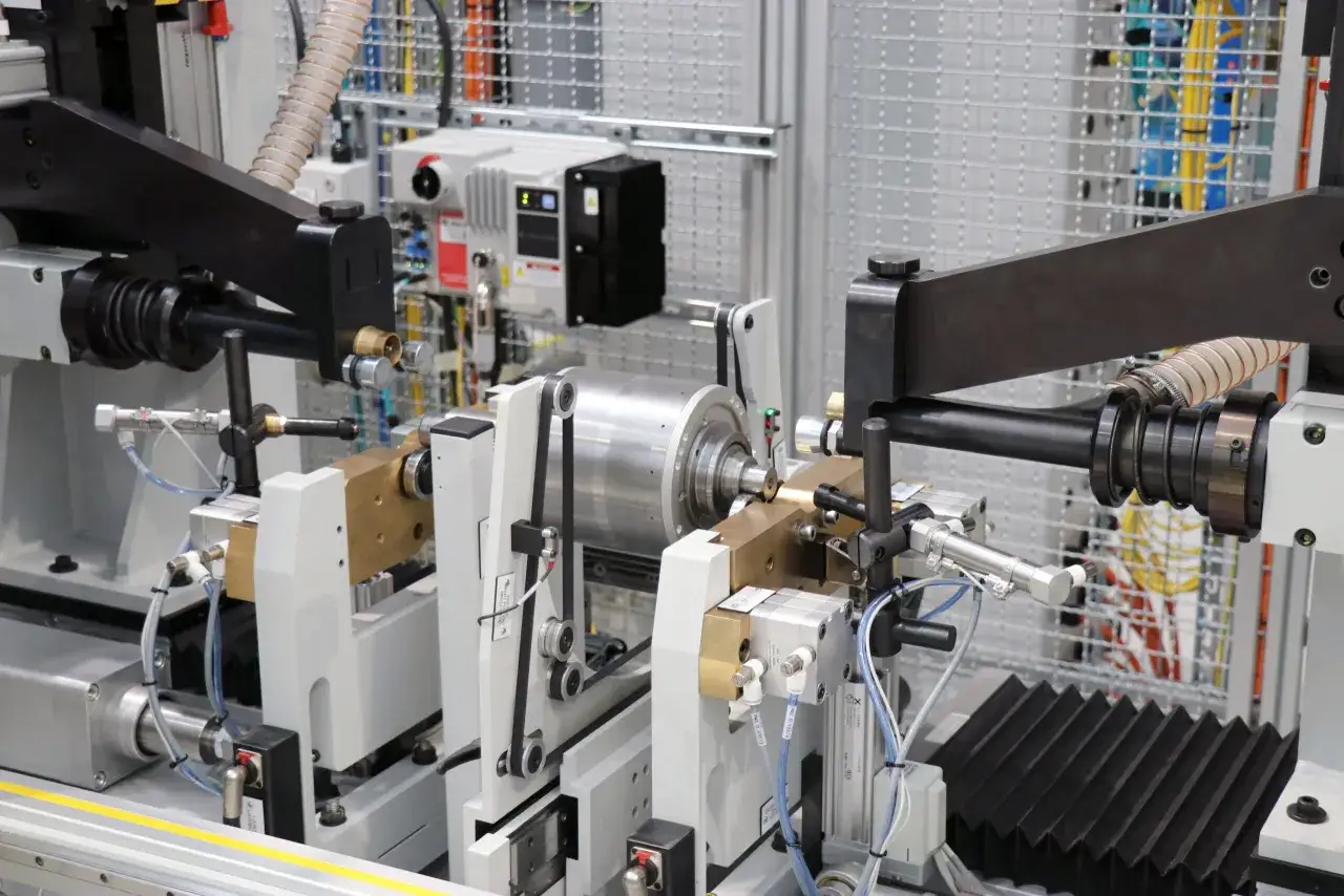 Precision machinery for electric motor balancing, featuring a rotating armature held by supports, belts, and sensors.